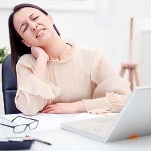 Collaboratrice en télétravail ressentant une douleur cervicale devant son ordinateur