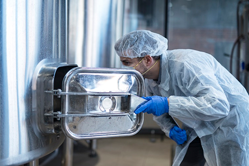 Technicien en blouse effectuant un contrôle qualité dans une cuve inox, illustrant la démarche Qualité Hygiène Environnement